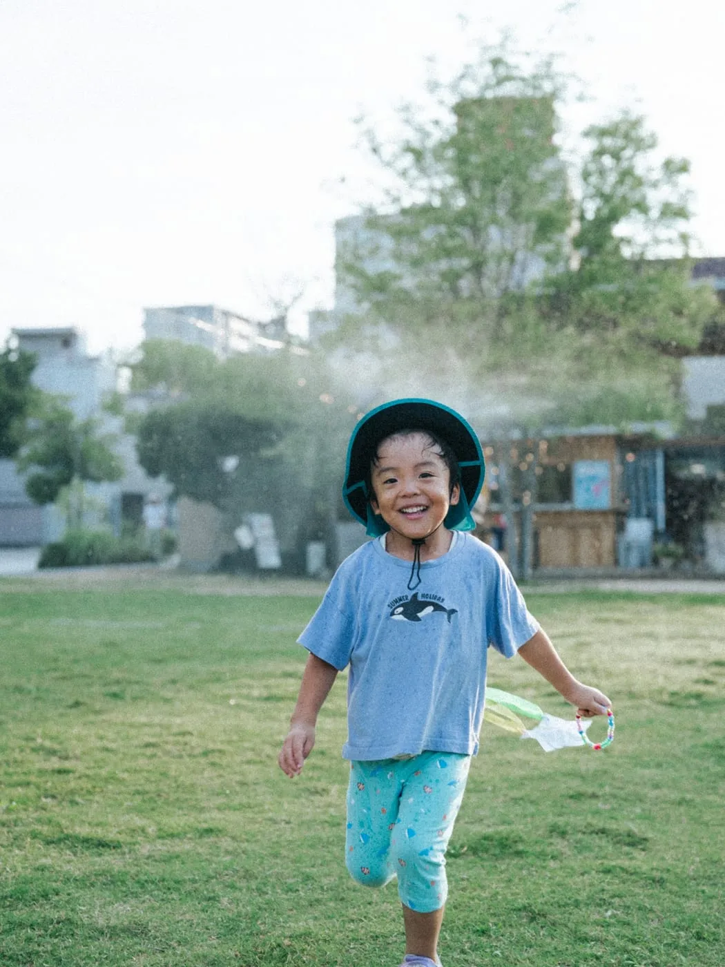 ミストの霧の中を走り抜ける子ども。芝生の広場と、奥にEnleeの建物が見える。